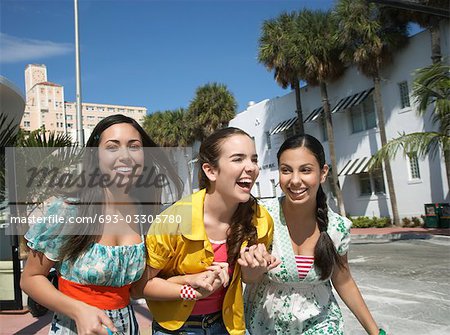 Three teenage girls (16-17) walking on street and laughing