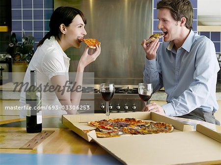 Jeune couple manger la pizza dans la cuisine
