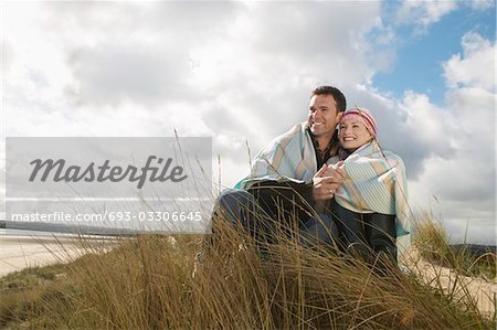 Couple wrapped in blanket embracing at ocean