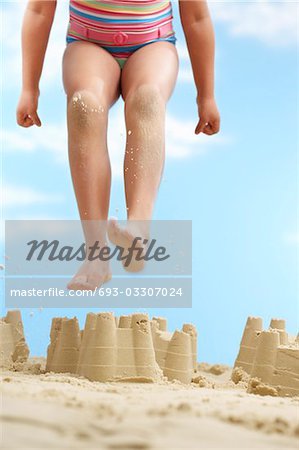 Girl (7-9 years) jumping on sand castle on beach, low section