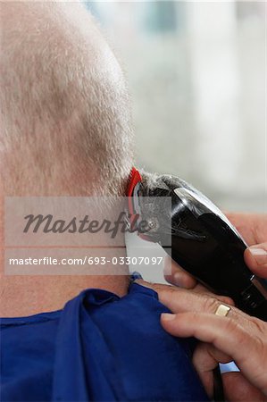 Barber shaving mans head in barber shop, close-up