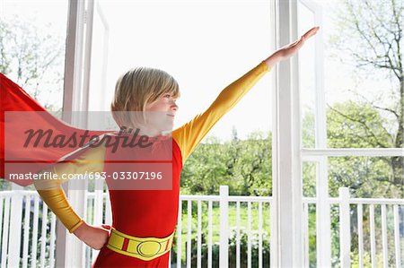 Portrait de porter costume de super héros garçon jeune (7-9), bras levé, à l'intérieur