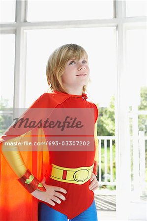 Portrait de jeune garçon (7-9) en costume de super héros, les mains sur les hanches, à l'intérieur