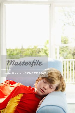 Young boy (7-9) sleeping in armchair, wearing superhero costume, indoors