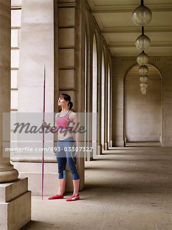 Female athlete holding javelin, standing in portico, portrait