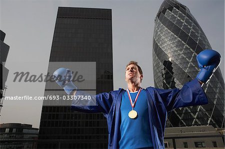 Boxer wearing gold medal standing in front of downtown skyscrapers, low angle view, London, England