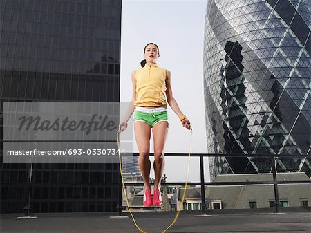 Femme à sauter sur la corde à sauter sur le toit du centre ville, vue d'angle faible, Londres