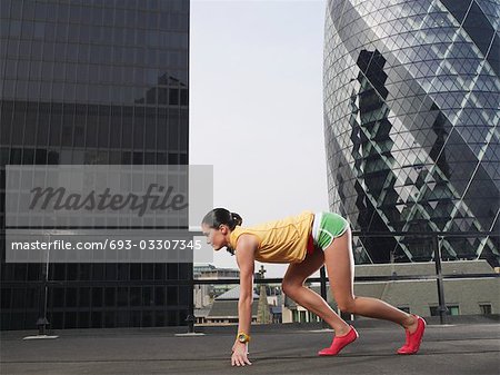 Woman crouching in starting position on downtown rooftop, side view, London, England