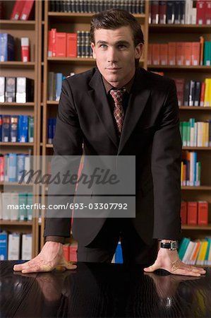 Man wearing suit leaning on desk in library, portrait