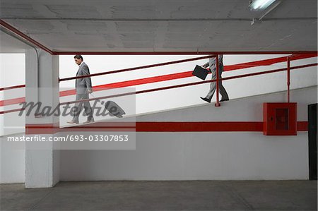 Two businessmen walking down ramp in parking garage with luggage