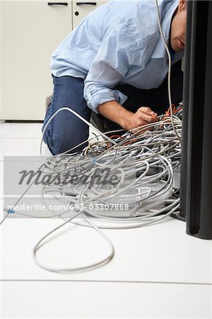 Man working on tangle of computer wires in office