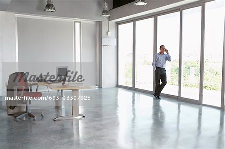 Homme à l'aide de téléphone portable, appuyé contre la fenêtre dans l'immeuble de bureaux vides