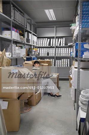 Woman using laptop, between boxes in storage room