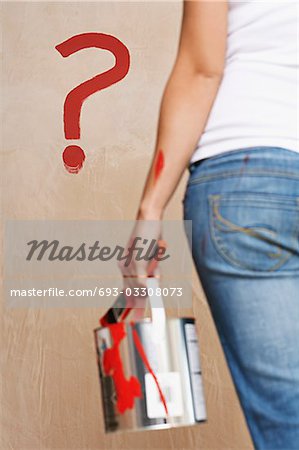 Woman holding painting can facing wall with painted question mark, mid section, back view
