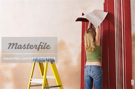 Woman hanging wallpaper, back view