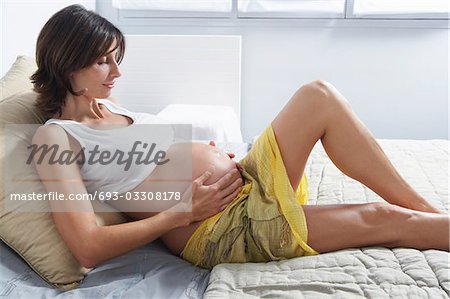 Pregnant woman holding stomach on bed in bedroom