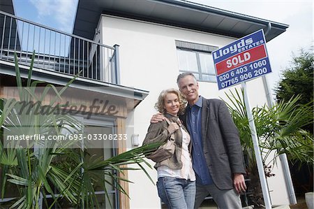 Couple faire place à l'extérieur de la nouvelle maison avec signe vendu, portrait