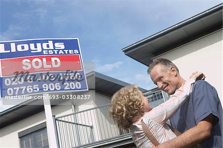Couple embracing outside new home with sold sign