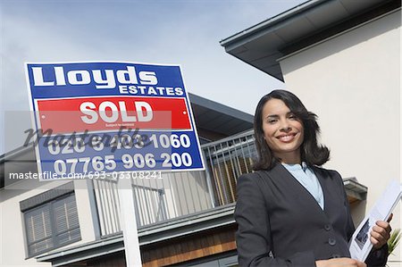 Real estate agent beside sold sign outside house, portrait