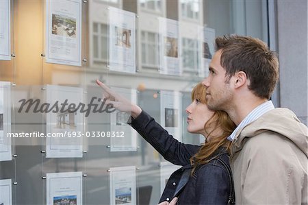 Couple à la recherche dans la fenêtre à l'extérieur des agents immobiliers