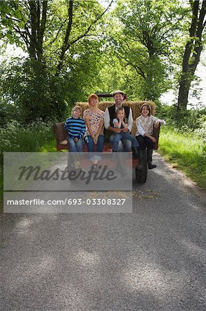 Parents with three children (5-9) sitting on trailer on country lane