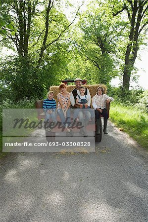 Parents with three children (5-9) sitting on trailer on country lane