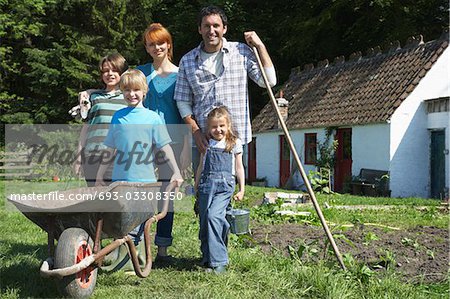 Parents with three children (5-9) gardening outside cottage, portrait