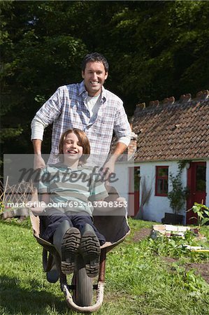 Father pushing son (7-9) in wheelbarrow outside cottage, portrait
