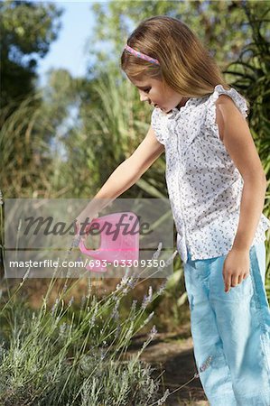 Girl (5-6) watering plant with plastic can