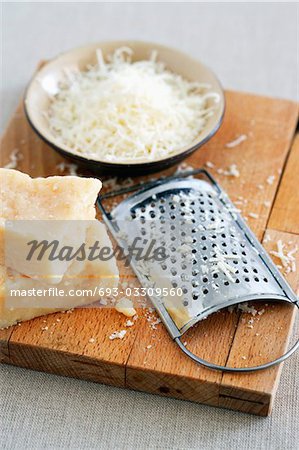 Parmesan cheese and grater on cutting board at table