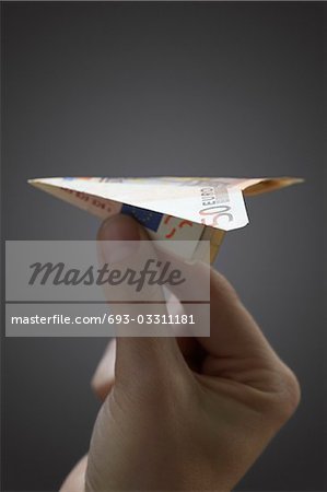 Person holding paper airplane made of 50 euro note, close-up of hand