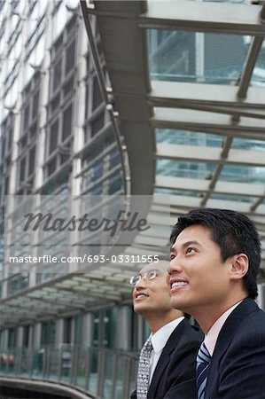 China, Hong Kong, two business men standing on footbridge, downtown, side view