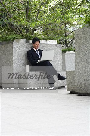 China, Hong Kong, business man sitting on stone bench using laptop