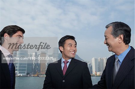 Three business men smiling, office buildings in background