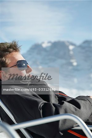 Man in winter coat and sunglasses sitting in arm chair by mountains