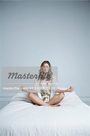 Jeune femme en robe de chambre méditant dans son lit