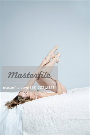 Young woman in underwear lying on bed with feet up