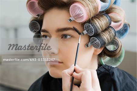 Model in Hair Curlers Having Makeup Applied