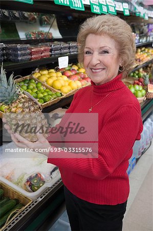 Senior woman holding pineapple in supermarket