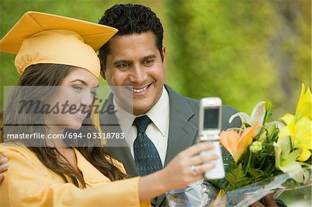 Graduate and father taking picture with cell phone outside