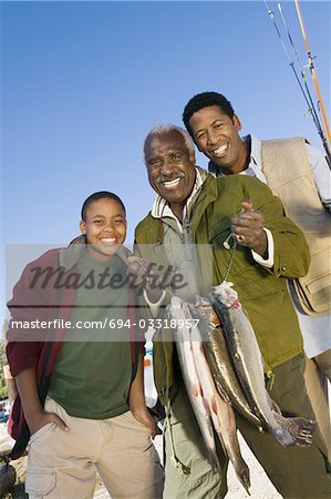 Male members of three generation family holding fishes, smiling, (portrait)