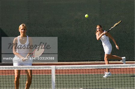 Doubles Player Hitting tennis ball with Forehand, team-mate standing at net