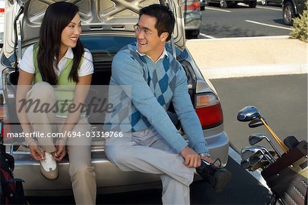 Couple Sitting on Rear Bumper of Car Putting on Golf Shoes