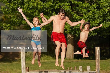 Deux enfants (7-9) main dans la main avec le père, jetant dans le lac.