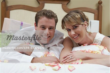 Bride and groom relaxing on bed among presents, portrait