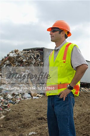 Worker standing near truck dumping waste at landfill site