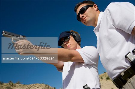 Instructor assisting woman aiming hand gun at firing range, low angle view