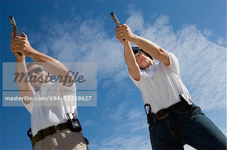 Man and woman aiming hand guns at firing range, low angle view