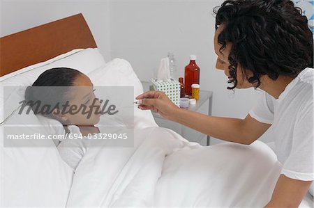 Nurse taking temperature of girl (7-9) lying in bed