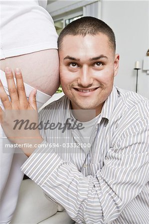 Smiling man with head at pregnant woman's abdomen